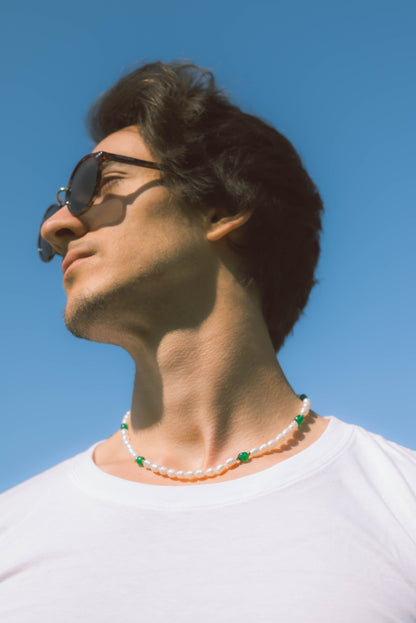 man wearing pearl necklace with green stones on a blue background