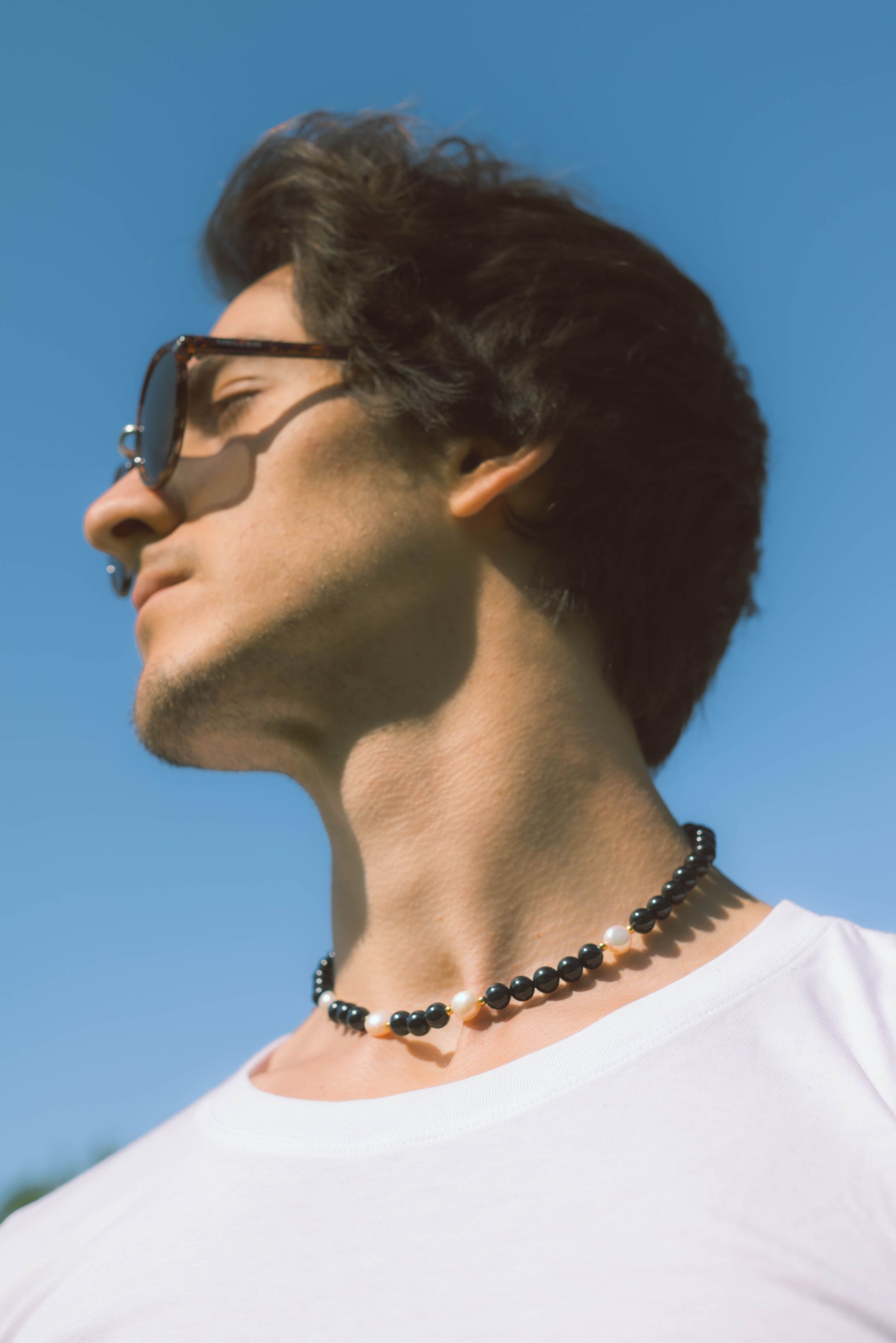 man wearing a black pearl necklace on a blue background