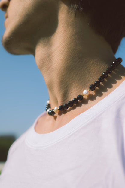 man wearing a black pearl necklace on a blue background