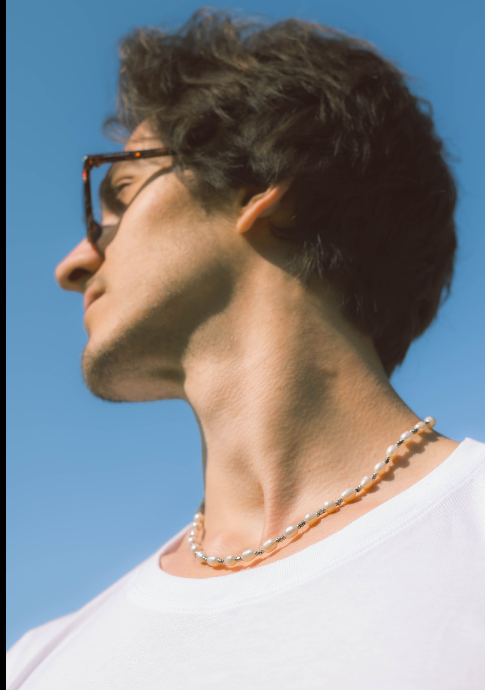 man wearing a pearl necklace with grey stones on a blue background