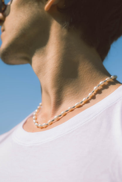 man wearing a pearl necklace with grey stones on a blue background