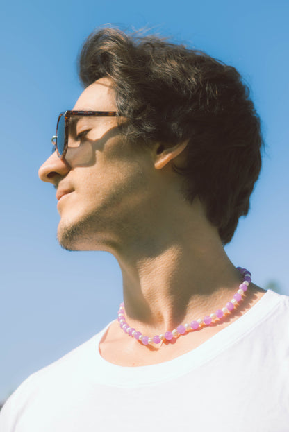 man wearing a pearl necklace with purple stones on a blue background