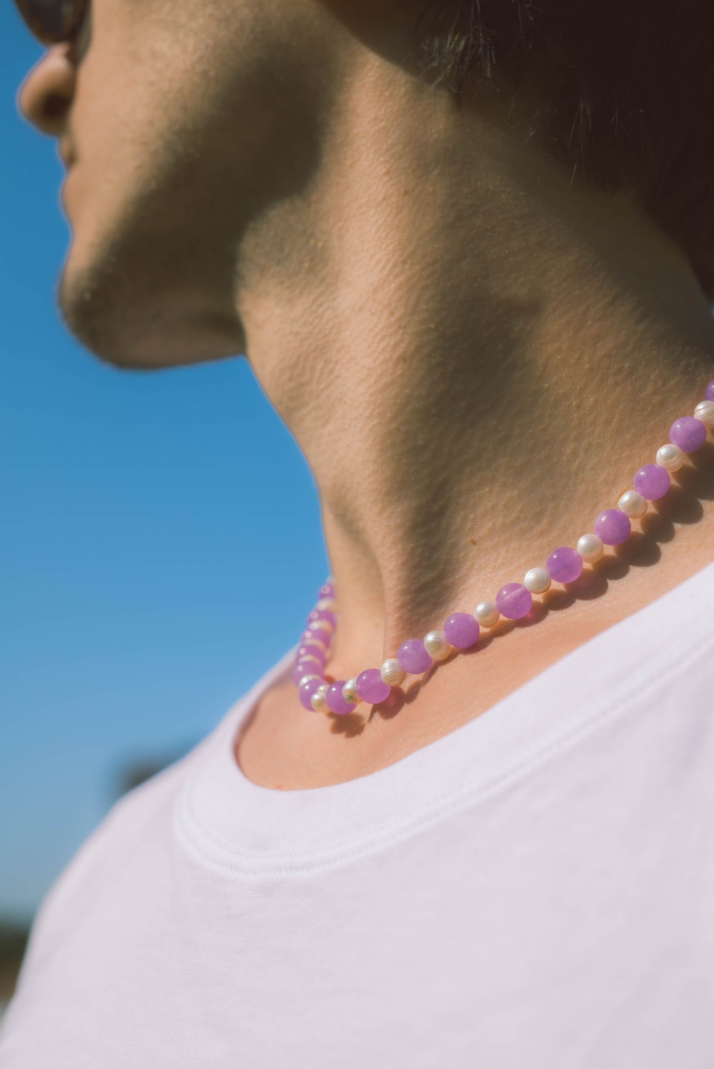 man wearing a pearl necklace with purple stones on a blue background