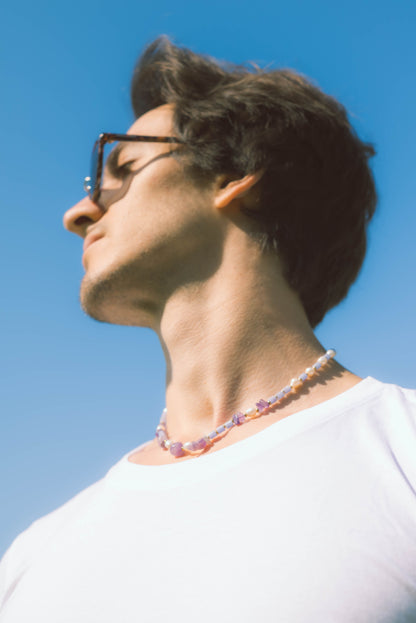 man wearing a pearl necklace with purple stones on a blue background