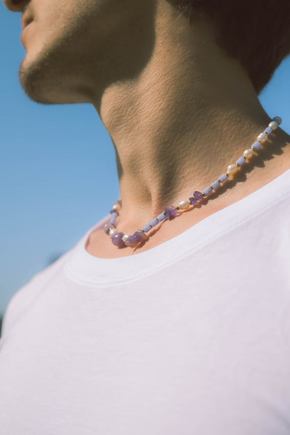 man wearing a pearl necklace with purple stones on a blue background