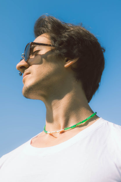 man wearing a green pearl necklace with the sky as a background