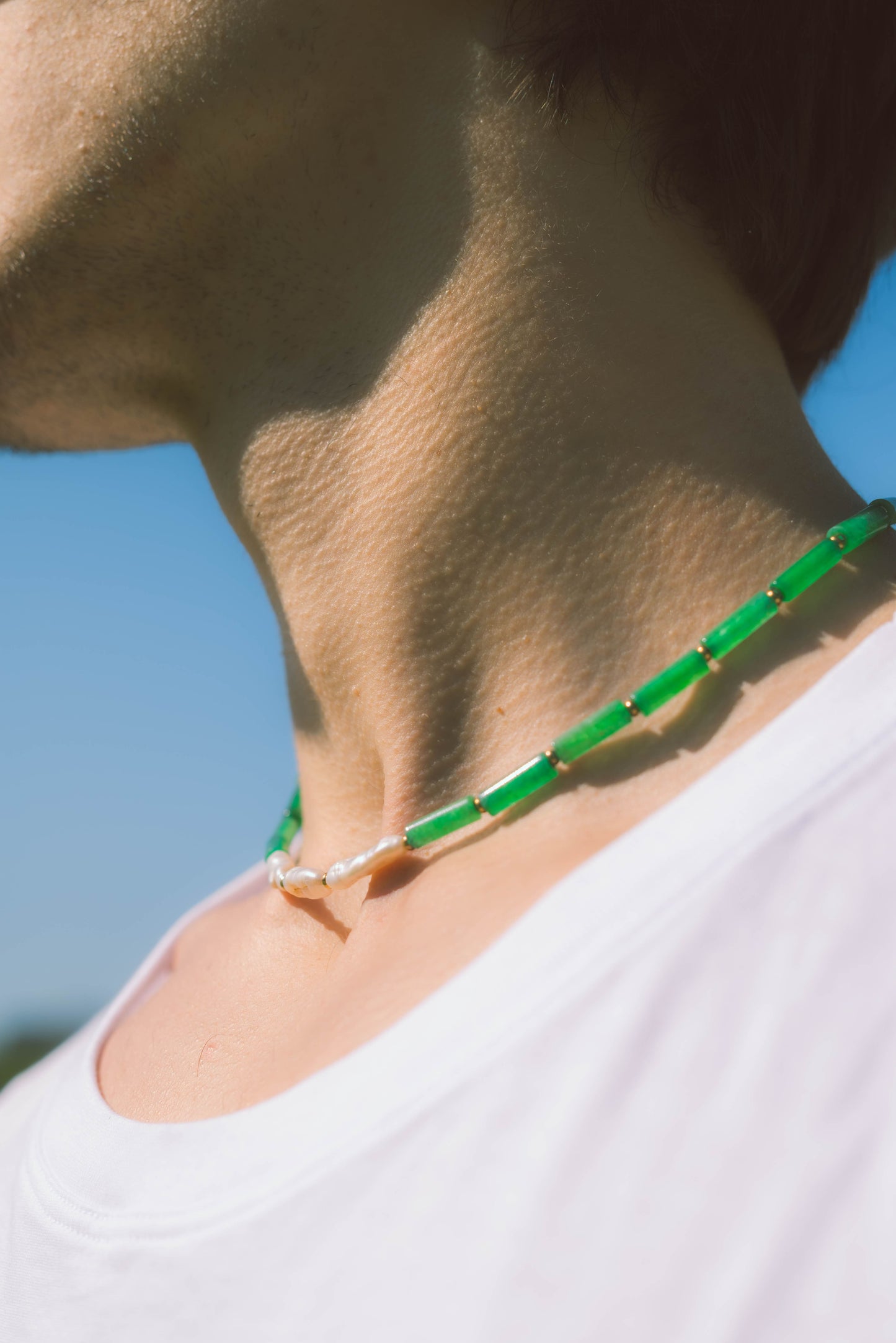 man wearing a green pearl necklace with the sky as a background