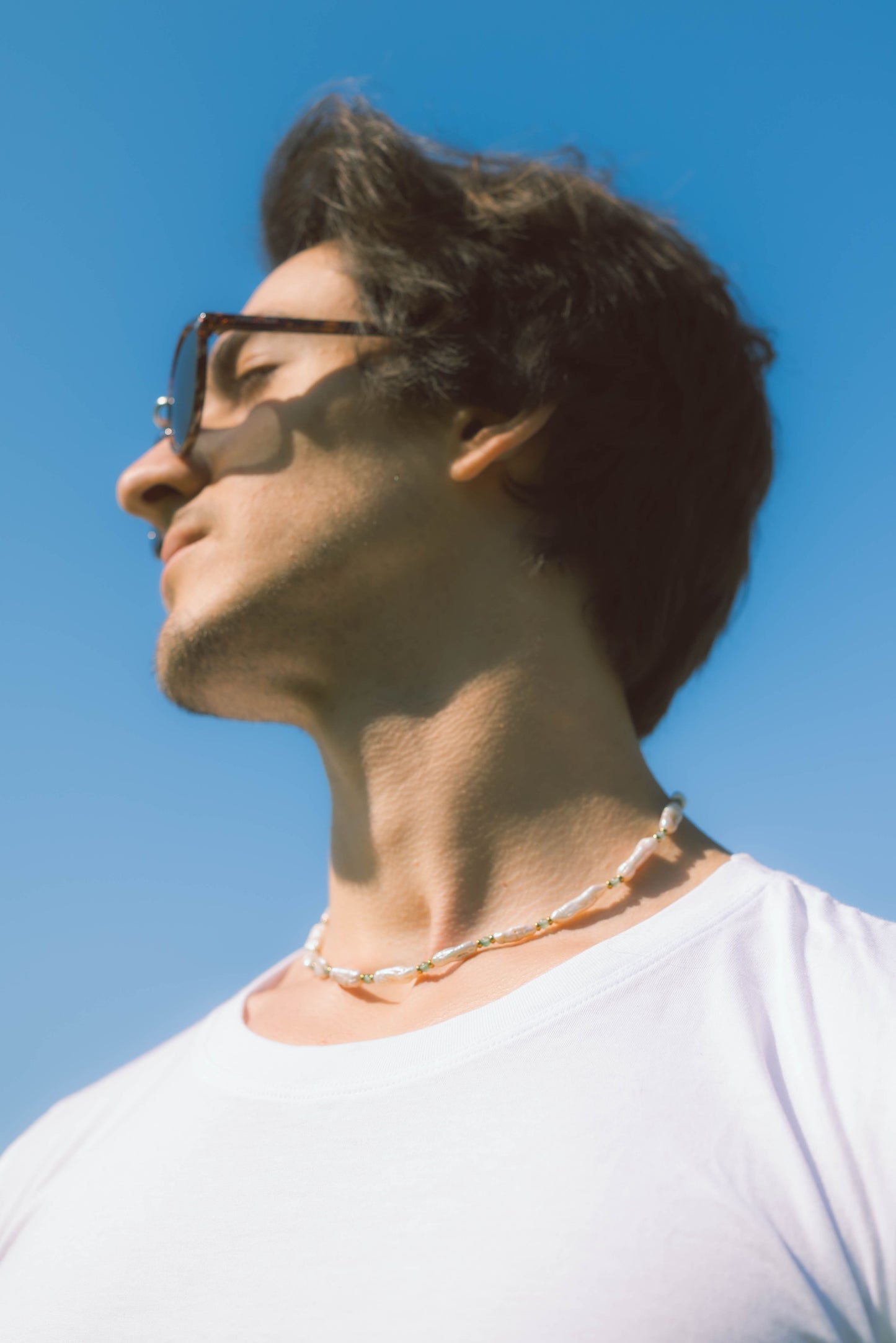 man man wearing a baroque pearl necklace on a blue background