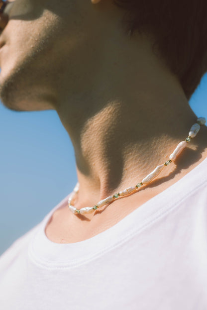 man man wearing a baroque pearl necklace on a blue background