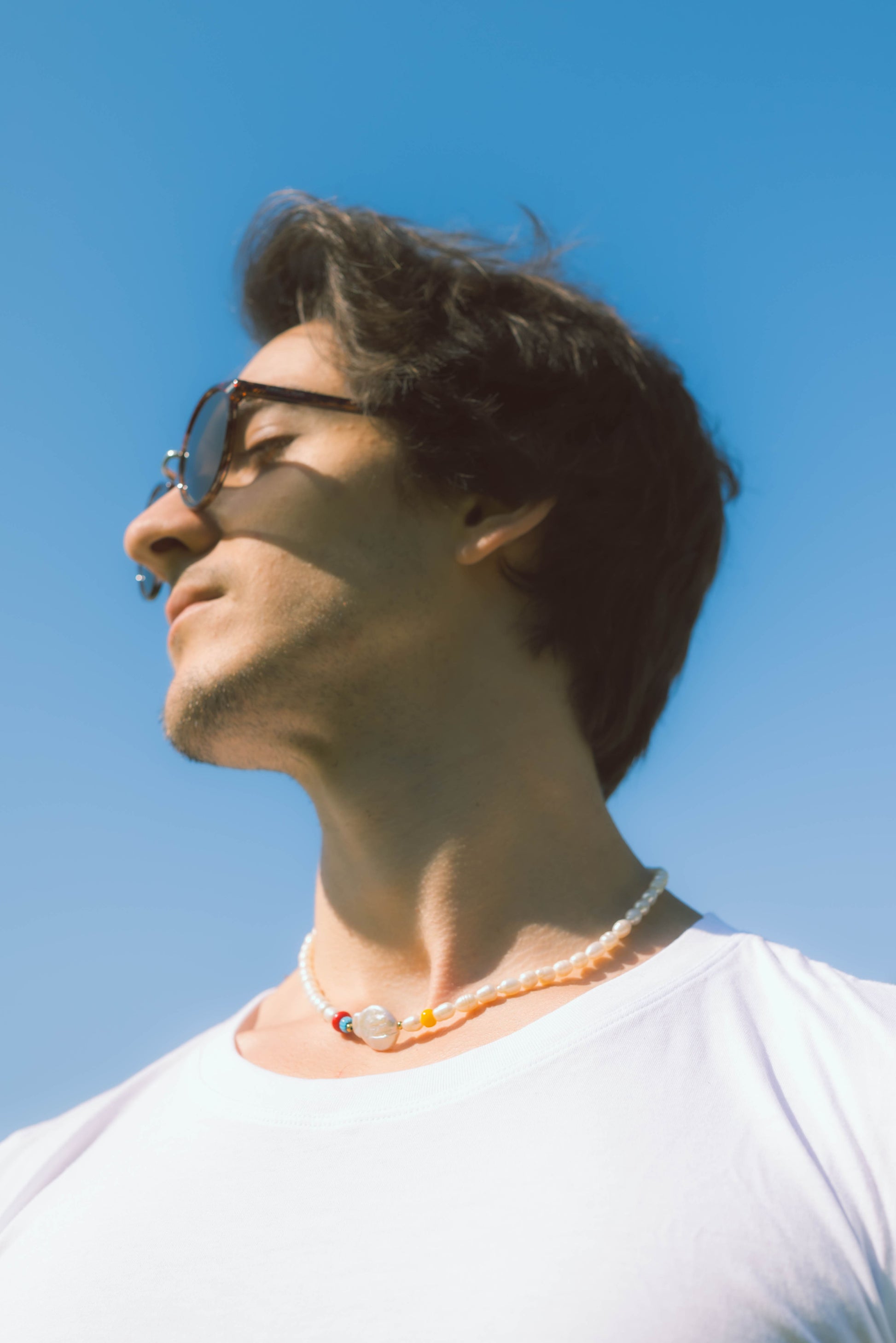 man wearing a baroque pearl necklace with color beads on a blue background