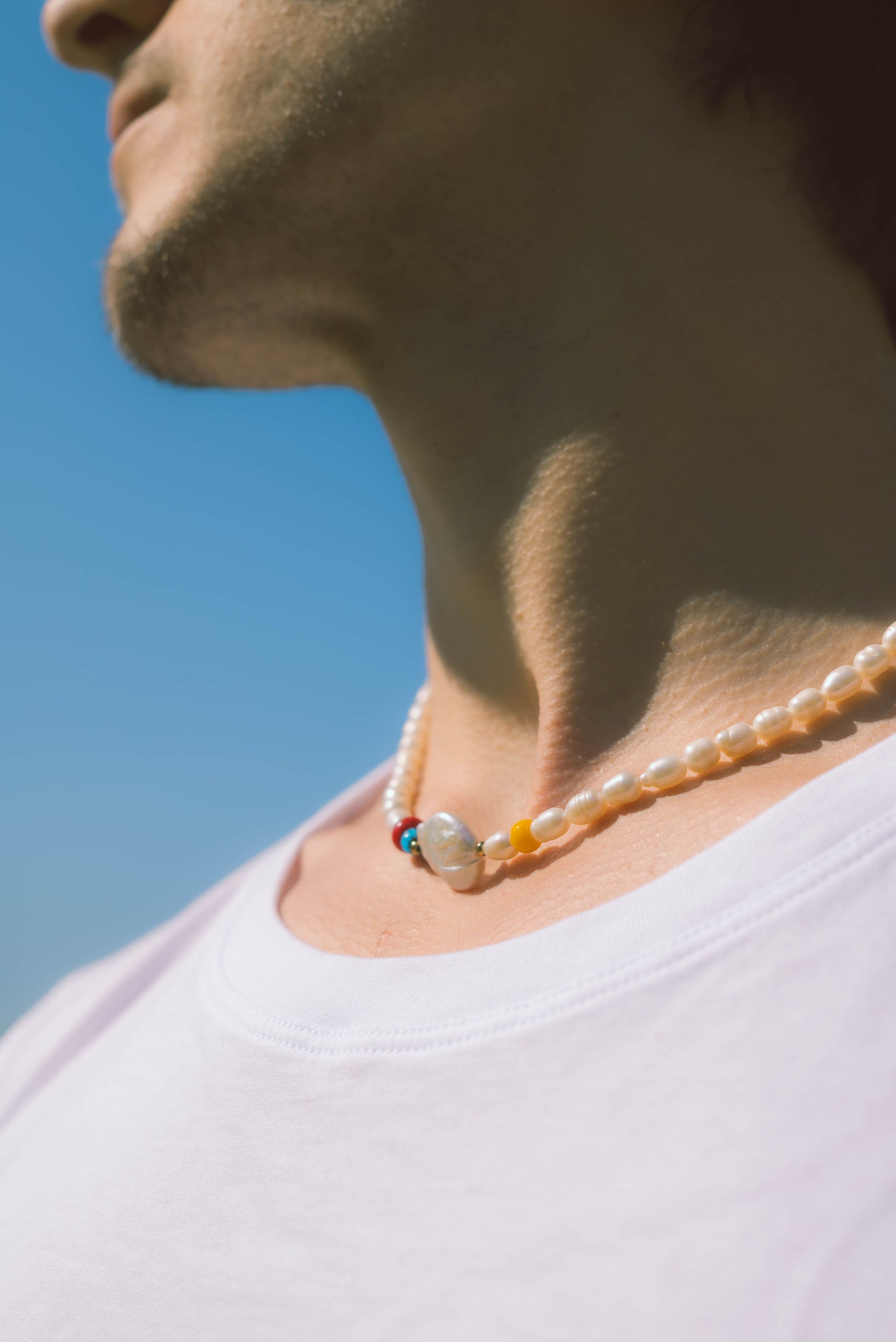 man wearing a baroque pearl necklace with color beads on a blue background