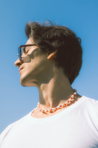 man wearing a red and white pearl necklace on a blue background